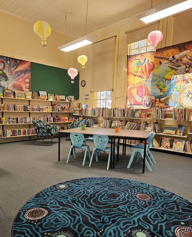 our well stocked library with desks and a colourful mat in the foreground. small hot air balloons are floating around the room