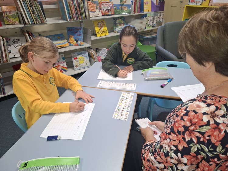 Our School Learning Support Officer working with two students. The students are both writing their spelling words