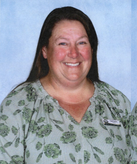 a female with long hair wearing a green flower print shirt smiling at the camera
