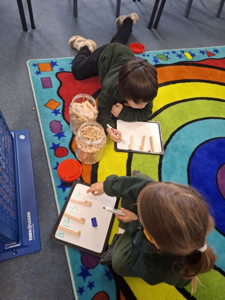two kindergarten students on a colourful rug working with blocks and a whiteboard during a Maths lesson