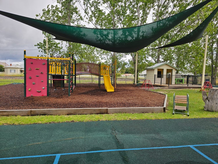 colourful play equipment with a slide, climbing frame and rock wall. There is a cubby house to the right.