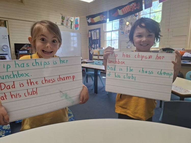 two happy students each holding a whiteboard while looking at the camera. they are showing some writing they have both completed during their writing lesson.
