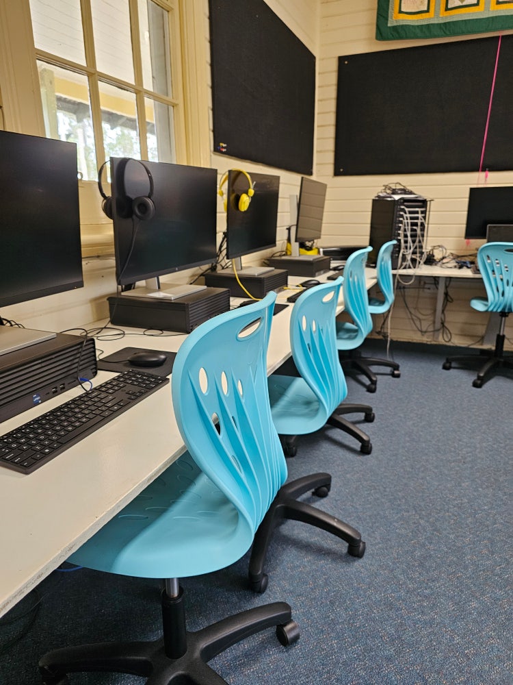 image of desktop computers on desks in the computer area. aqua coloured chairs in front of the computers