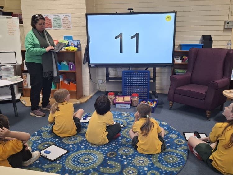 teacher teaching maths on a big screen while students look on