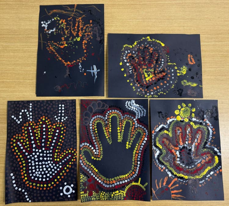 image showing five hand prints on black card. Around each hand, students have used sticks to paint dots creating a indigenous inspired artwork using red, yellow and white paint